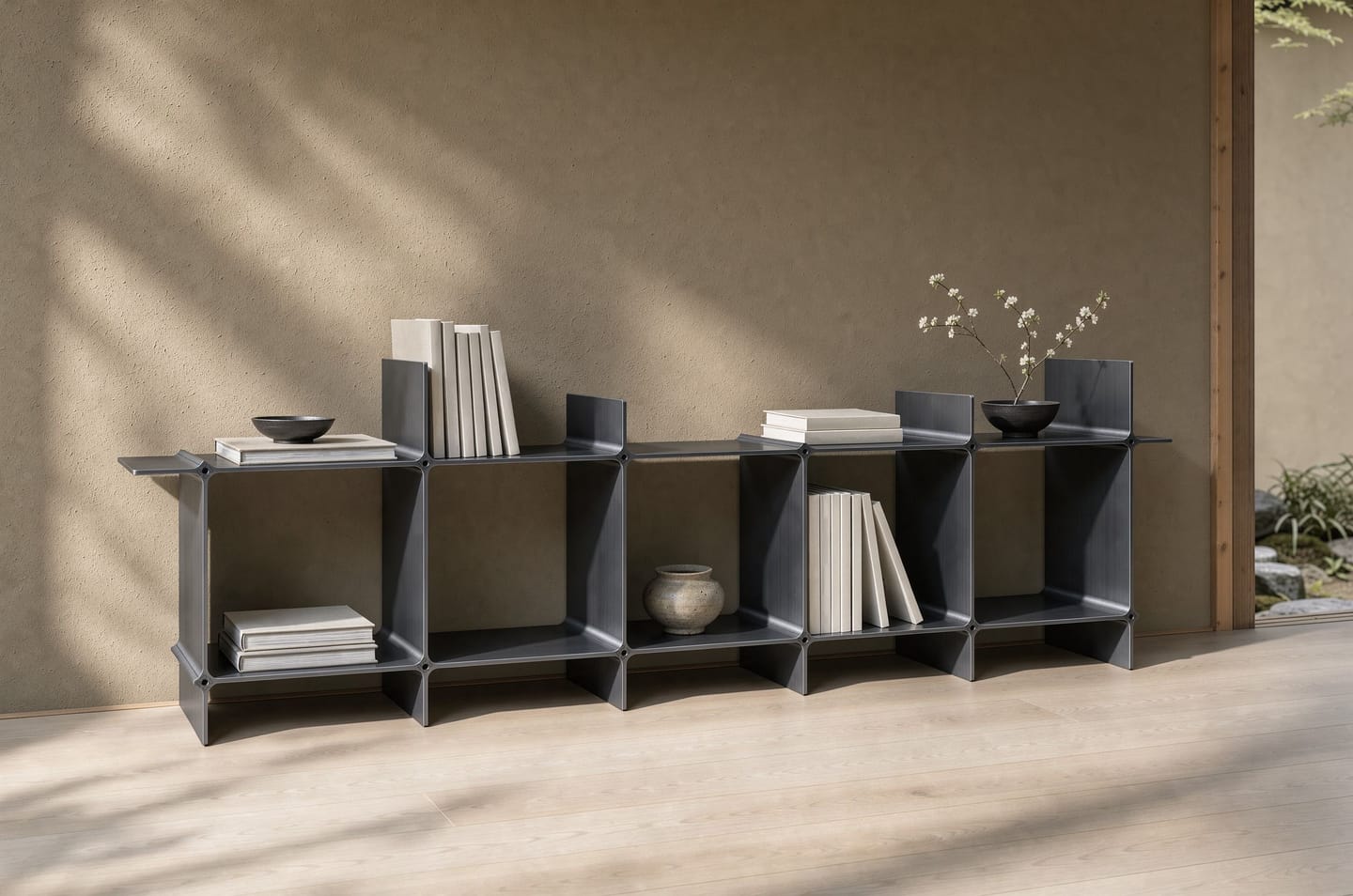 Montique as a long sideboard in black — five compartments in a row, books between the upright wings, against a clay-plastered wall; on the right the view into the garden