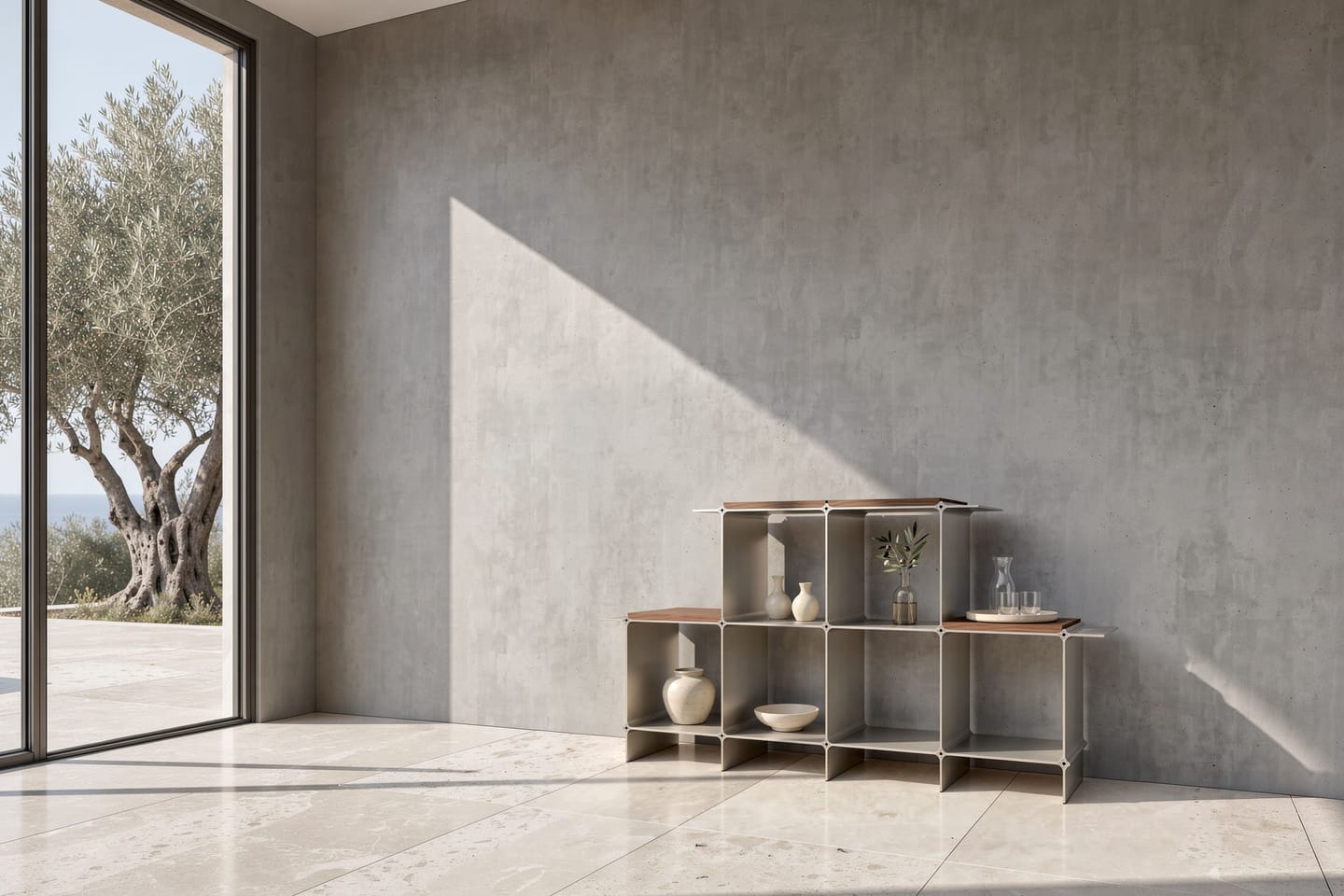 Montique shelving system in gold with wooden shelves in walnut — against a concrete wall, on the left the open glass front to the terrace with an olive tree and the sea