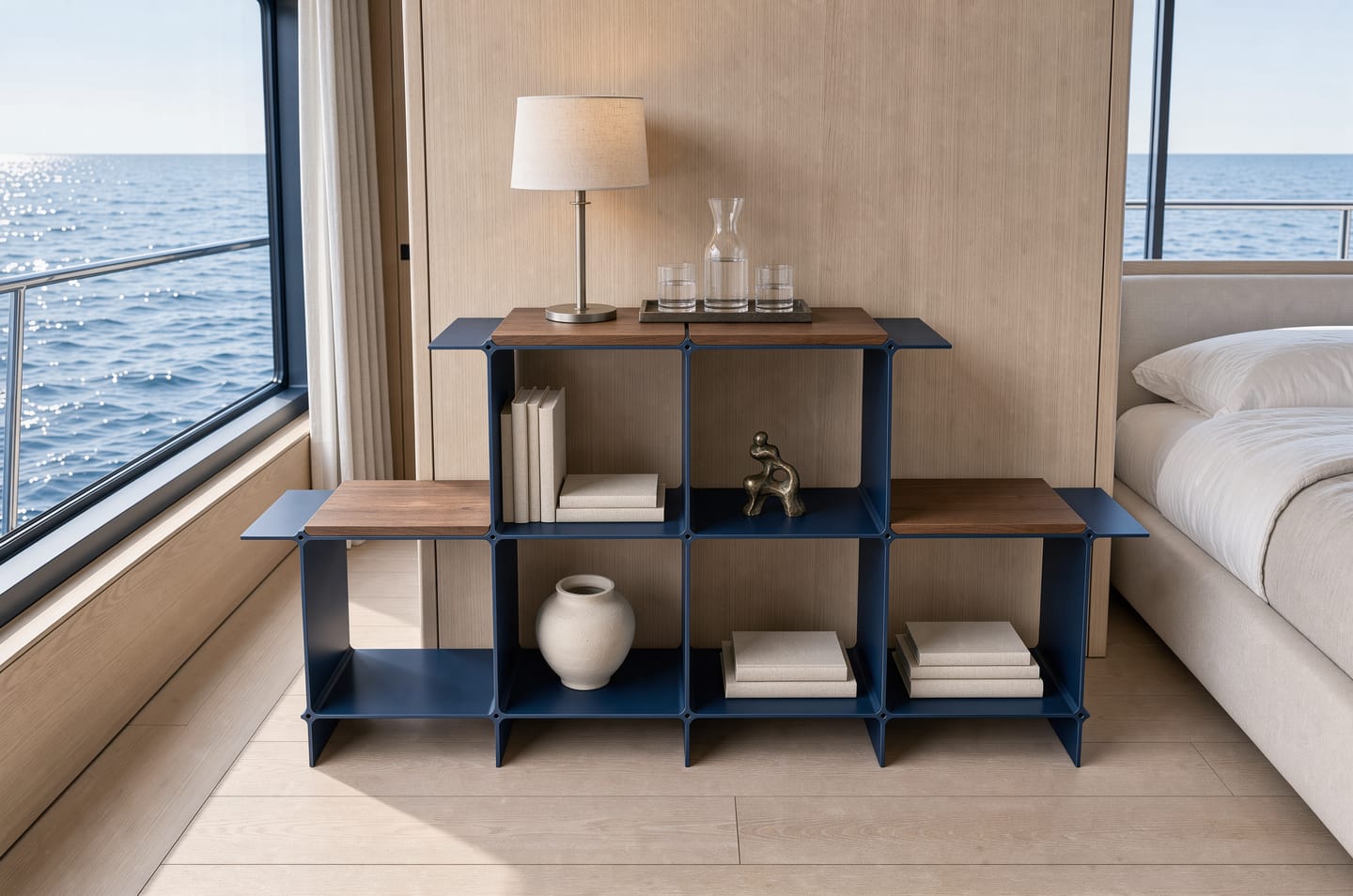 Montique shelving system in dark blue with wooden shelves in walnut, a table lamp and a carafe on top — in a cabin with oak panelling, the sea outside the window