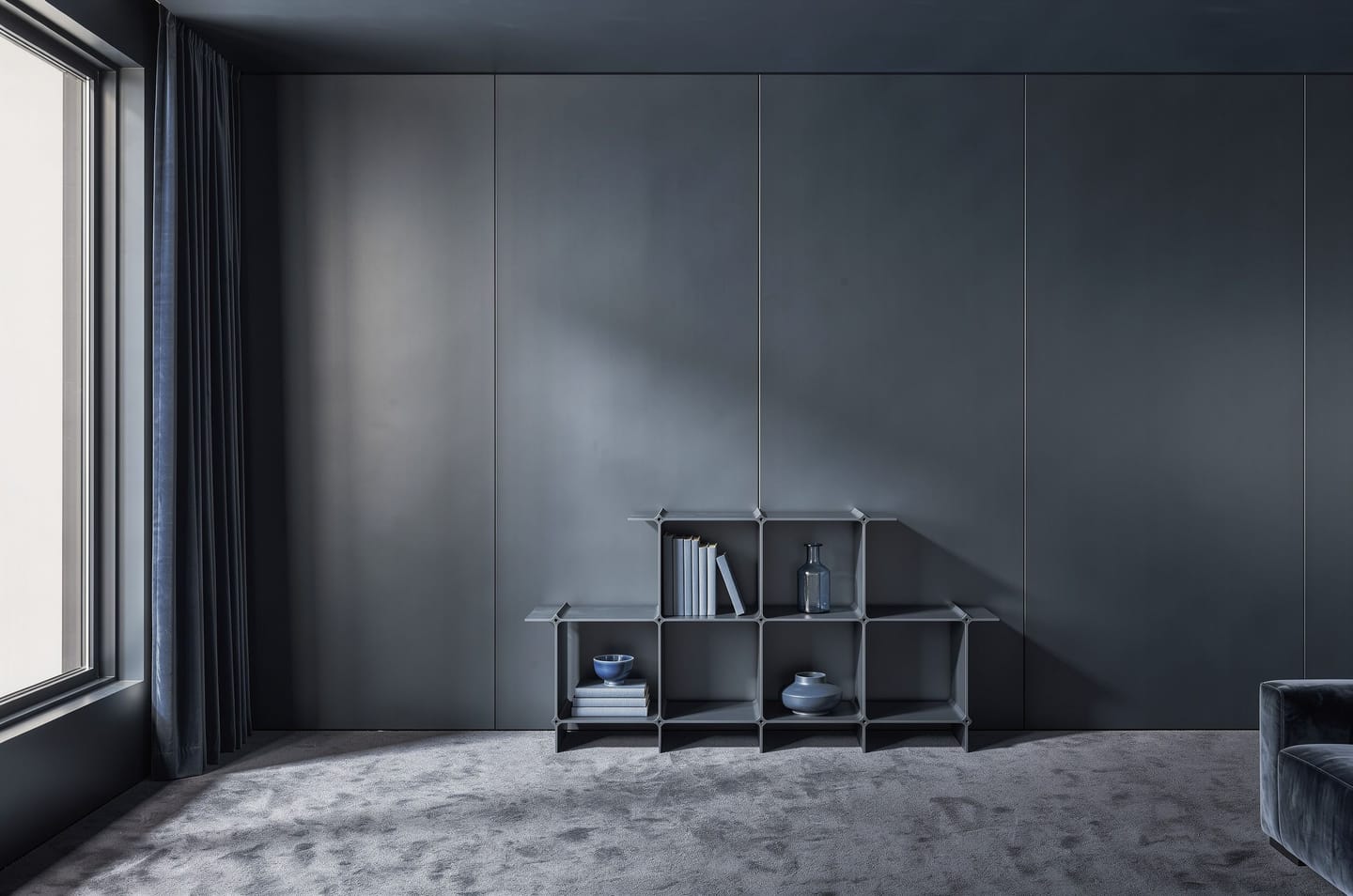 Shelf in dark blue with books and vessels in a room entirely in blue